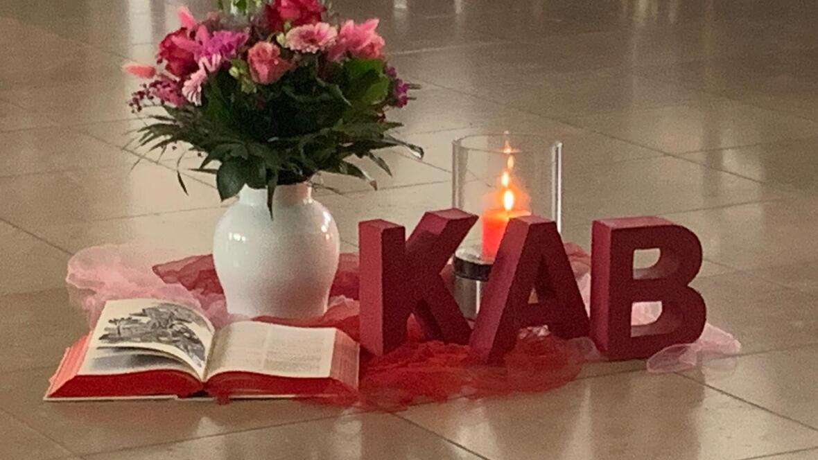 Blumenvase mit rosa Gerbera und Rosen, eine Bibel und KAB Buchstaben auf einem Tuch